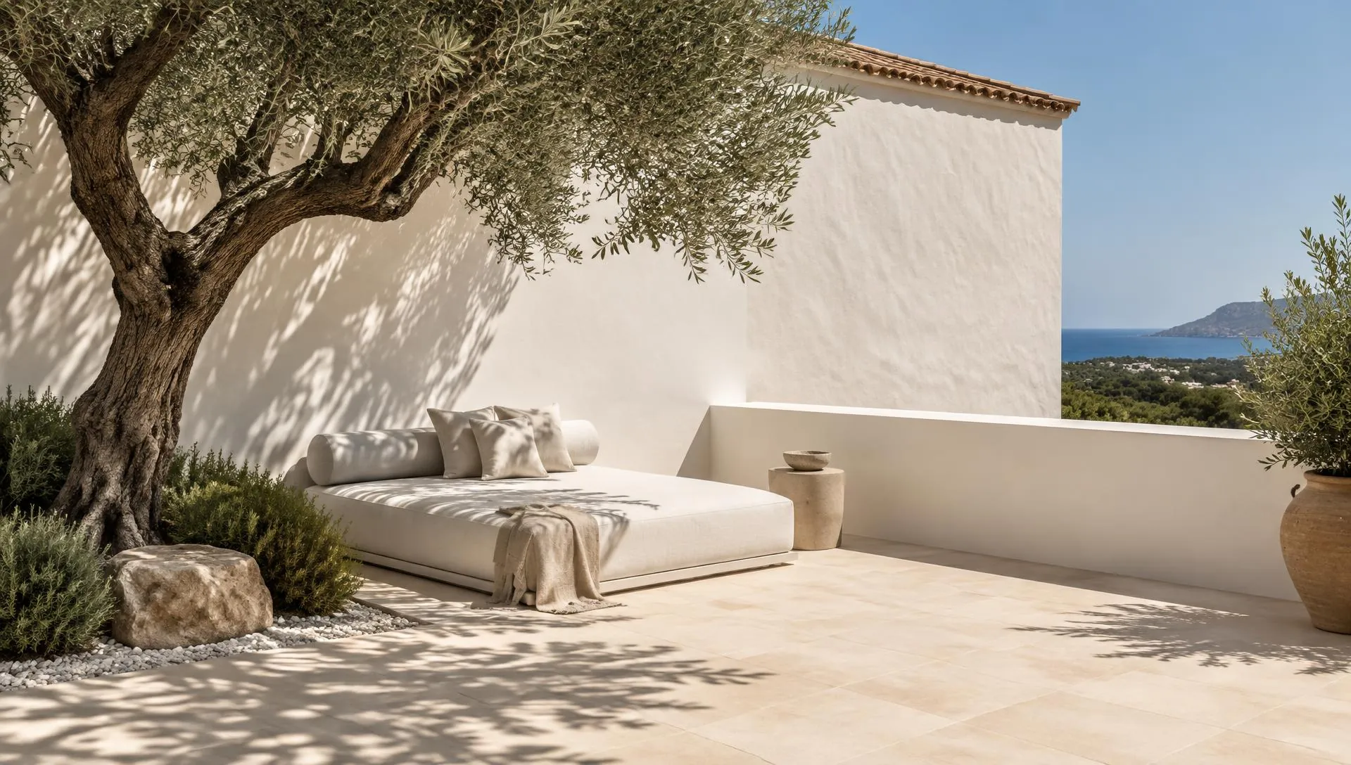A sunlit Algarve outdoor living terrace with linen seating, an olive tree and a distant sea view
